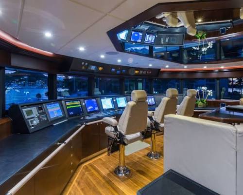 A superyacht bridge with navigation screens, wood consoles and cream leather helm chairs